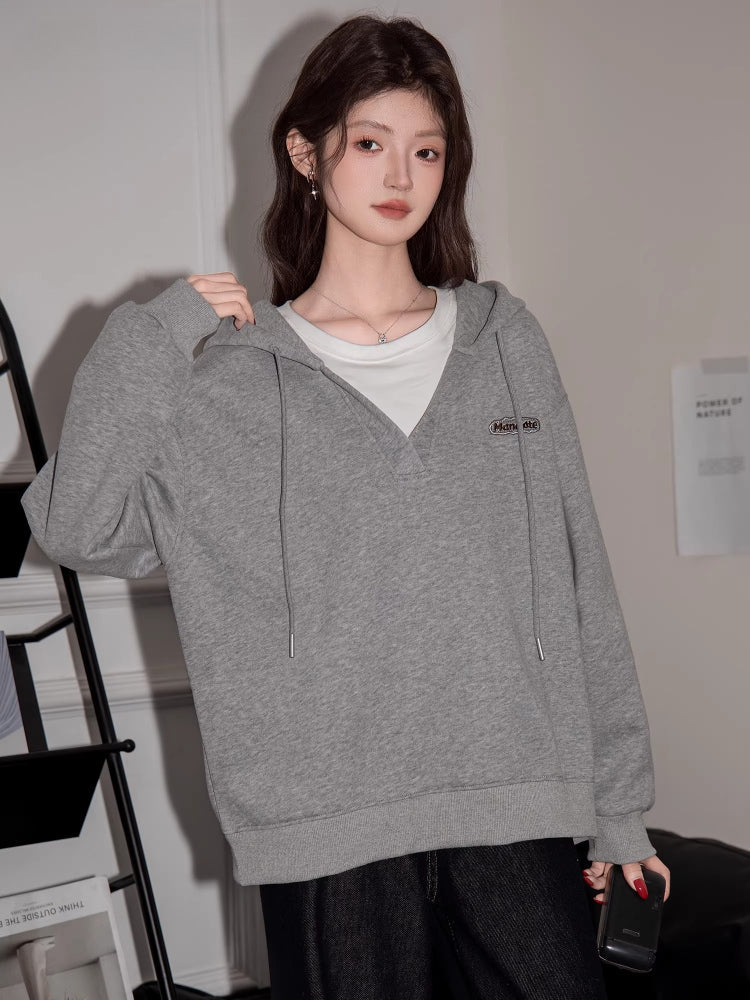 Woman wearing a grey V-neck oversized hoodie and black jeans, posing with a handbag.