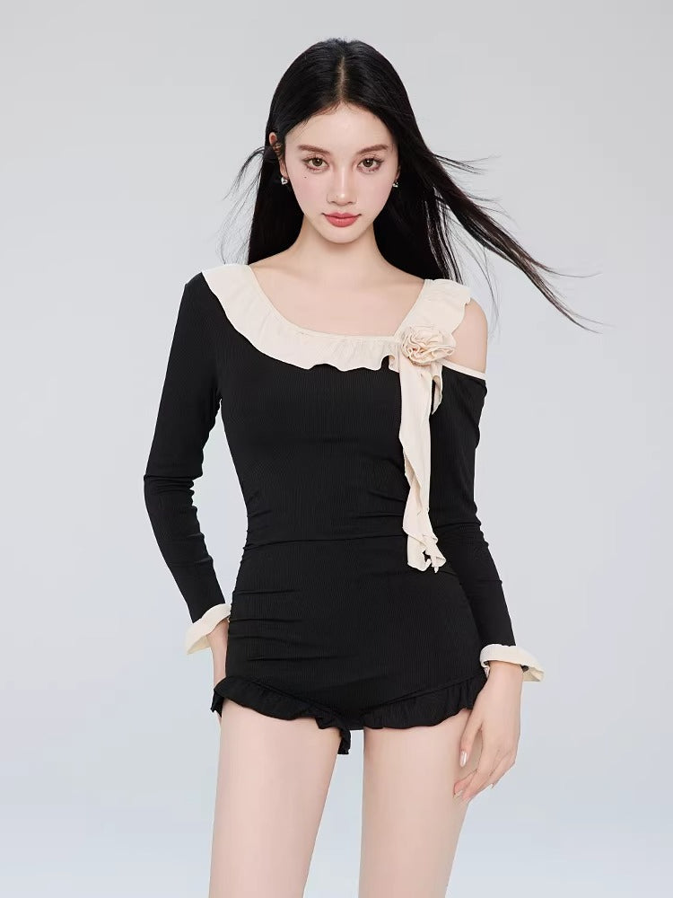 Front view of a woman wearing a black long-sleeved one-piece swimsuit with an asymmetrical neckline and ruffle trim.