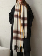 Full body shot of a woman wearing a long dark coat and a large plaid scarf with white, brown, and yellow stripes.