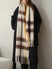 Full body shot of a woman wearing a long dark coat and a large plaid scarf with white, brown, and yellow stripes.