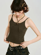 Woman wearing a dark olive green halter crop top with a ring detail at the neckline, pulling at the hem.