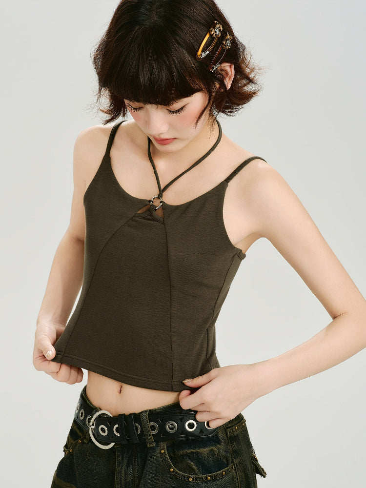 Woman wearing a dark olive green halter crop top with a ring detail at the neckline, pulling at the hem.