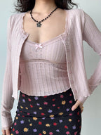 Woman wearing a pink cropped knit cardigan with lace trim and a floral print skirt, showing the full outfit.