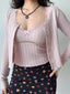 Woman wearing a pink cropped knit cardigan with lace trim and a floral print skirt, showing the full outfit.