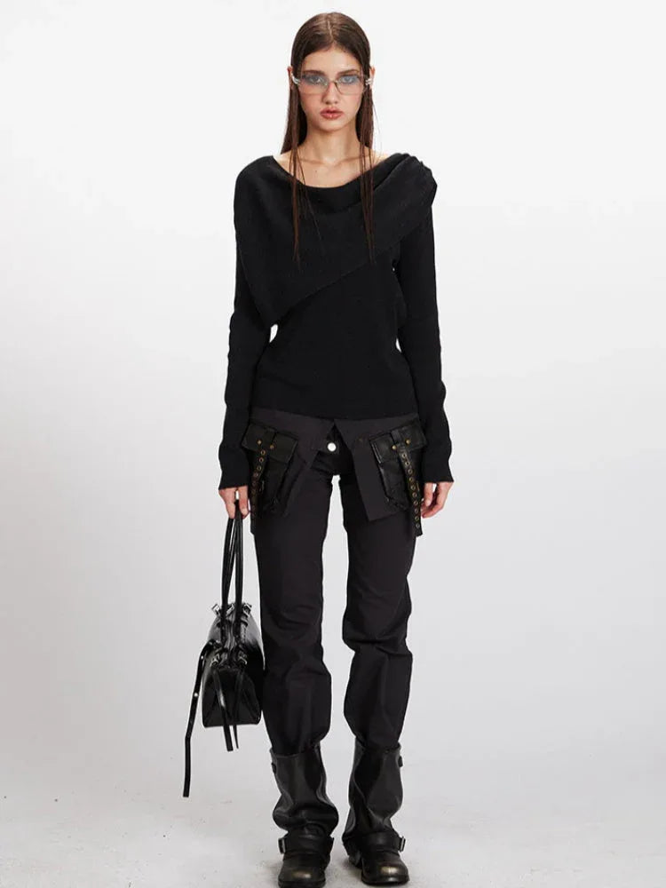 Full body shot of a woman wearing a black asymmetrical knit sweater and black cargo pants.