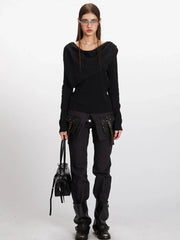 Full body shot of a woman wearing a black asymmetrical knit sweater and black cargo pants.