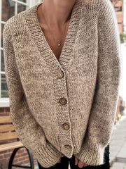 Woman standing outdoors, wearing a beige V-neck cardigan.