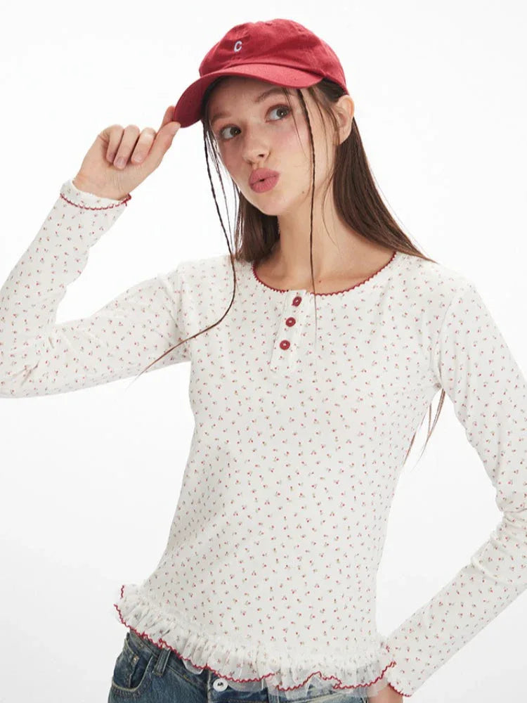Model posing with a red baseball cap and a white long-sleeve top with a floral print and red trim.