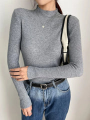 Woman wearing a gray ribbed mock neck long sleeve sweater with blue jeans and a black belt
