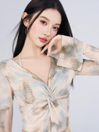 Close-up of a woman's face and upper torso, showcasing the abstract print and sheer mesh fabric of a long-sleeve top.