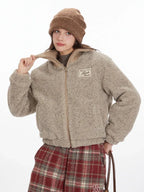 Close-up of a model adjusting the collar of a beige fuzzy bomber jacket.
