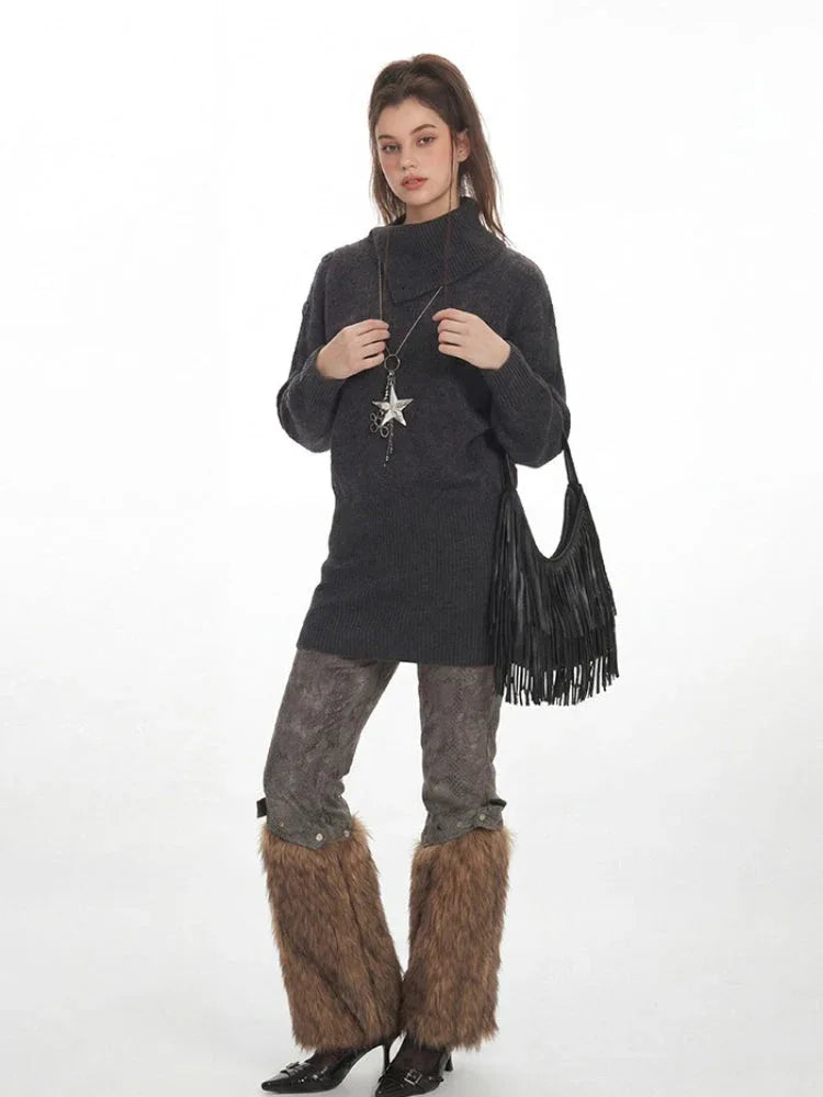 Full-body shot of a woman in a charcoal grey oversized turtleneck knit tunic, patterned leggings, and brown furry leg warmers, accessorized with a star pendant necklace and a black fringed handbag.