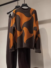A brown and orange abstract patterned oversized sweater and dark pants hanging on a rack.