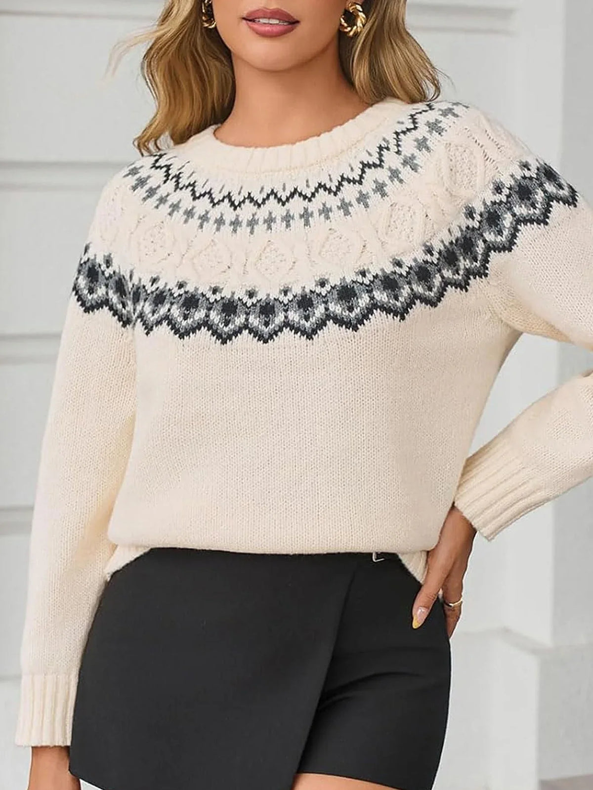 Woman wearing a cream-colored knit sweater with a Fair Isle pattern around the yoke and black trousers.