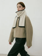 Woman walking in a beige textured coat and cream scarf with black trim, paired with black pants