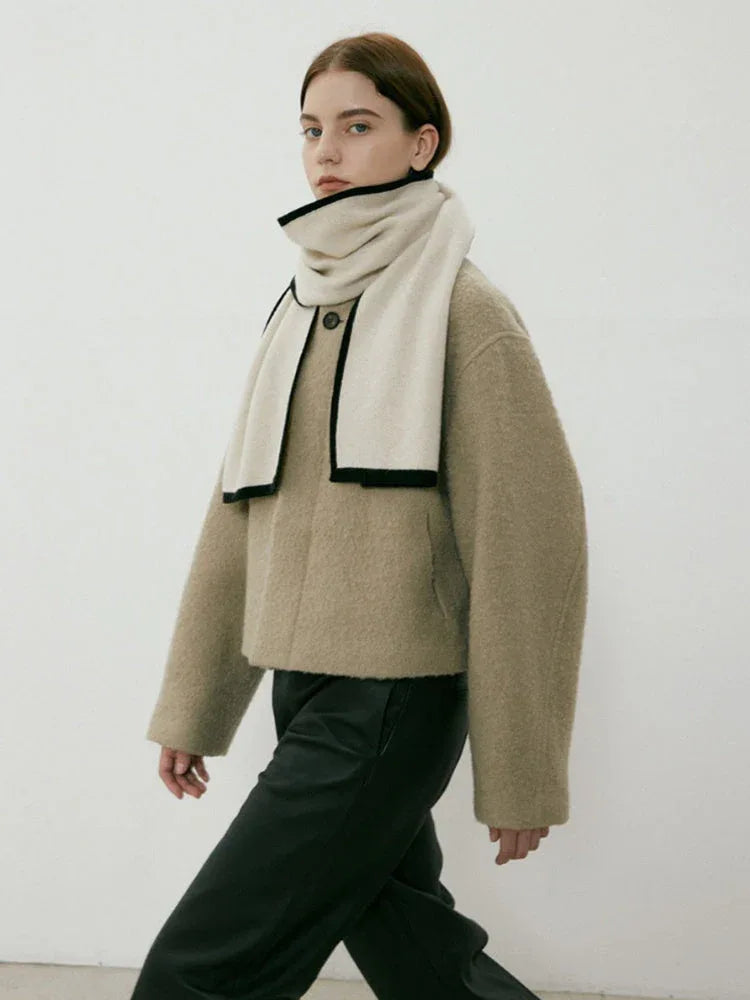 Woman walking in a beige textured coat and cream scarf with black trim, paired with black pants