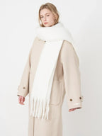 Woman wearing a white fluffy scarf draped over a beige coat, angled front view