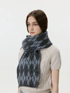 Close-up of a woman wearing a cream cable-knit sweater and a grey and black argyle scarf