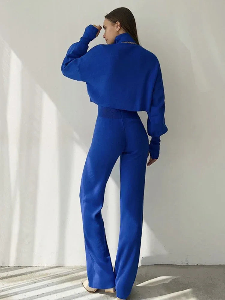 Back view of a woman wearing a blue knit two-piece set, highlighting the silhouette of the cropped sweater and pants.