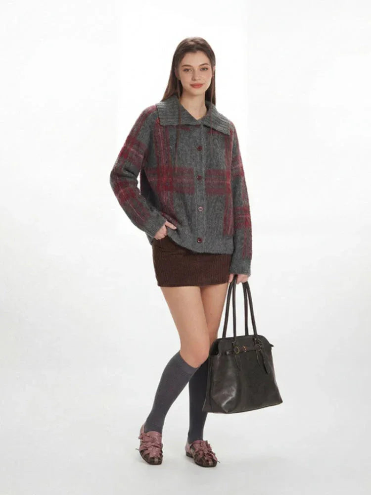 Full body shot of a woman in a grey plaid knit jacket, brown mini skirt, and grey knee-high socks, holding a black handbag.