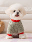 A fluffy white Bichon Frise dog sits facing forward, wearing a light green fleece dog jumpsuit with red cuffs and collar. The dog has its tongue slightly out and is looking at the camera.