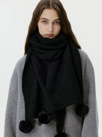 Close-up of a woman wearing a black knit scarf with pom-pom embellishments