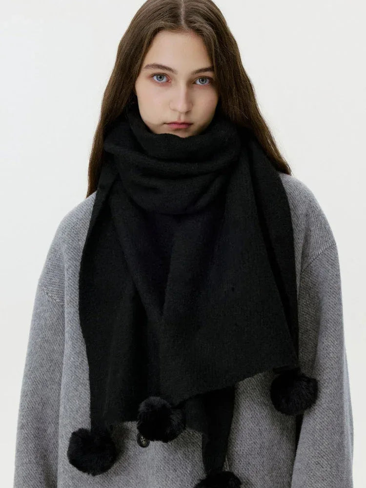 Close-up of a woman wearing a black knit scarf with pom-pom embellishments