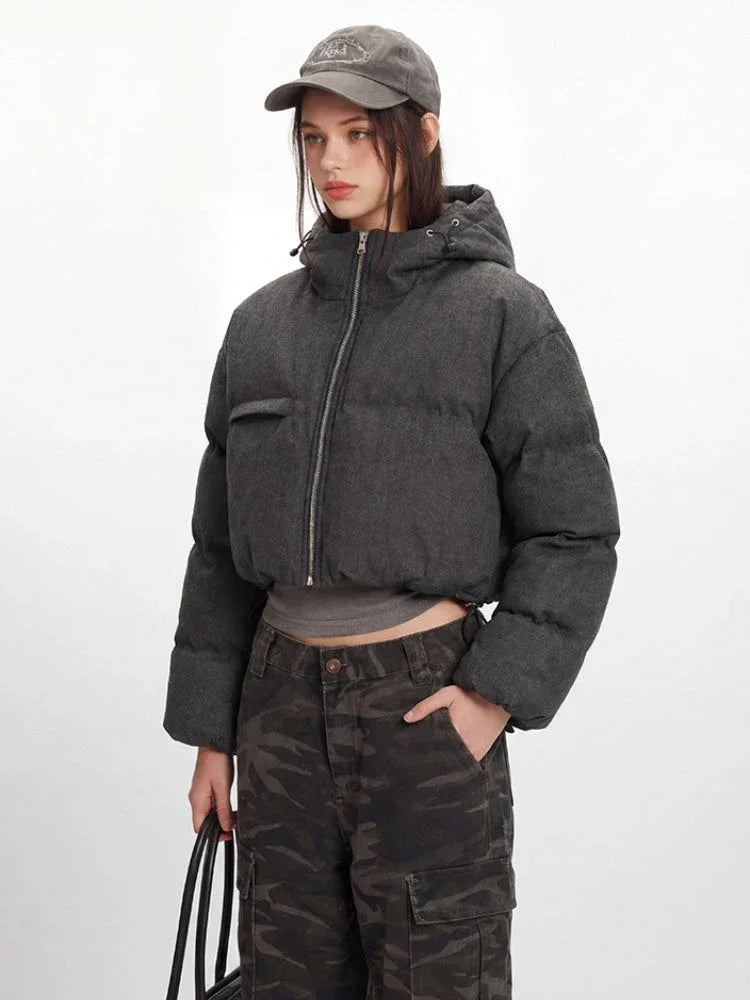Another angle of a model in a cropped grey puffer jacket, grey long-sleeved shirt, and camouflage cargo pants, with one hand in her pocket.