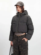 Another angle of a model in a cropped grey puffer jacket, grey long-sleeved shirt, and camouflage cargo pants, with one hand in her pocket.