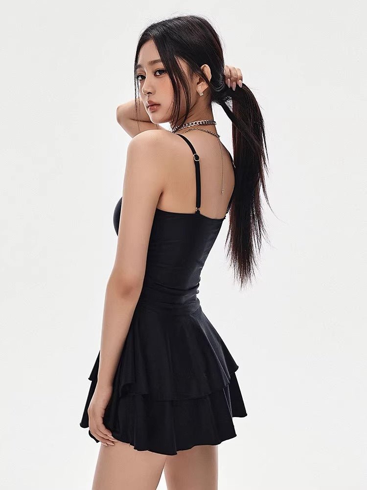Rear view of a woman wearing a black asymmetrical cutout dress with a tiered skirt, holding her hair in a ponytail.