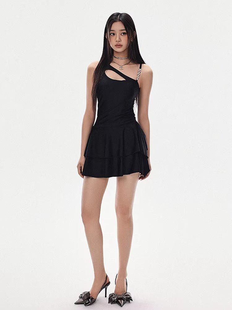 Woman in a black asymmetrical cutout dress with a tiered skirt and high heels, standing and looking forward.