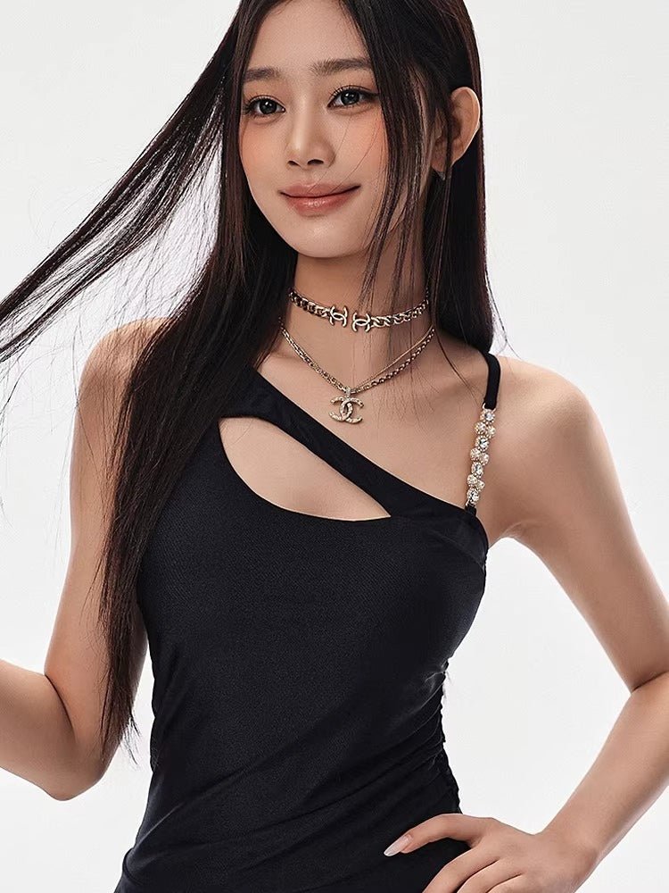 Close-up of a woman's upper body wearing a black asymmetrical cutout dress with layered necklaces.