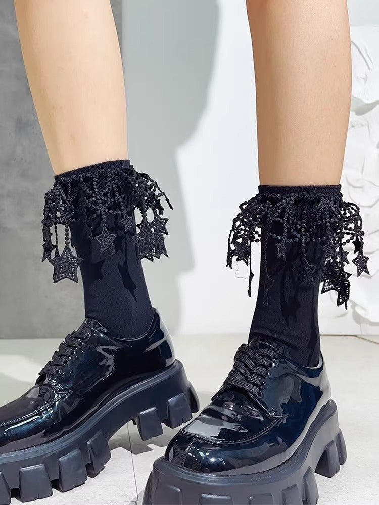 Close-up of feet wearing black ankle socks with intricate lace and star embellishments, paired with chunky black platform shoes.