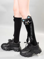 Close-up of knee-high black socks featuring a black cat charm with blue ears and dangling legs.