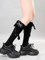 Knee-high black socks with a plush black cat charm dangling from the side of the leg, paired with chunky black sneakers.