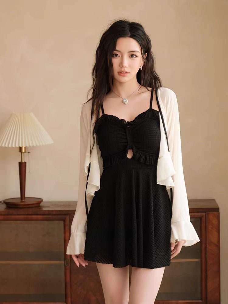 Woman in a black one-piece swimsuit and white cover-up, posing