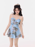 Woman wearing a blue tie-dye print swimsuit with ruffled trim and a flared skirt, posing against a white background.