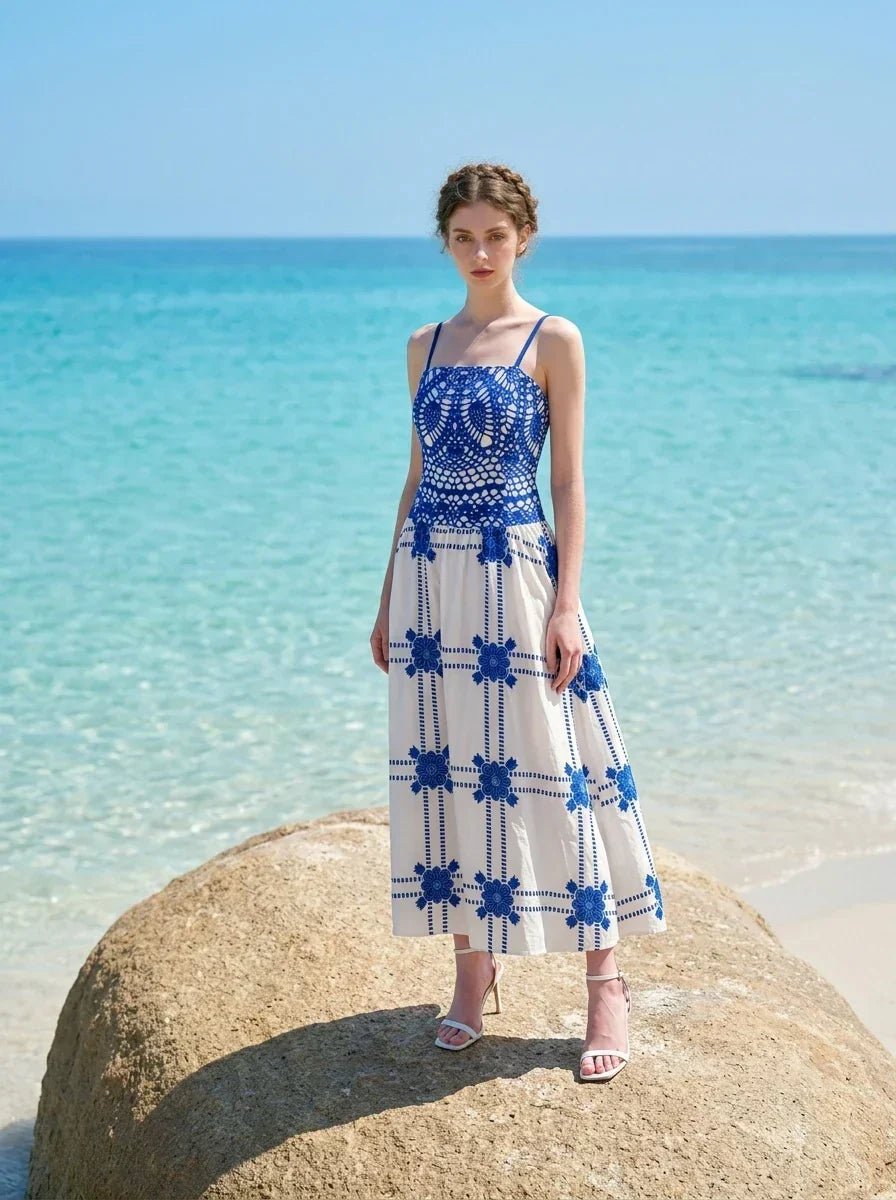 Woman wearing a blue and white crocheted and embroidered maxi dress standing on a large rock at the beach.