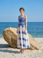 Woman wearing a blue and white crocheted and embroidered maxi dress standing on a beach near a large rock.