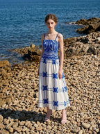 Woman wearing a blue and white crocheted and embroidered maxi dress standing on a rocky beach.