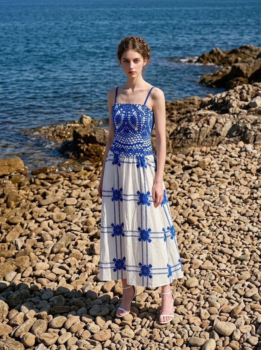 Woman wearing a blue and white crocheted and embroidered maxi dress standing on a rocky beach.