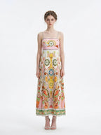 Woman wearing a white maxi dress with a colorful paisley print and pink smocked bodice, standing against a white background.