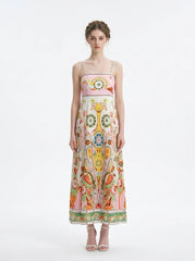 Woman wearing a white maxi dress with a colorful paisley print and pink smocked bodice, standing against a white background.
