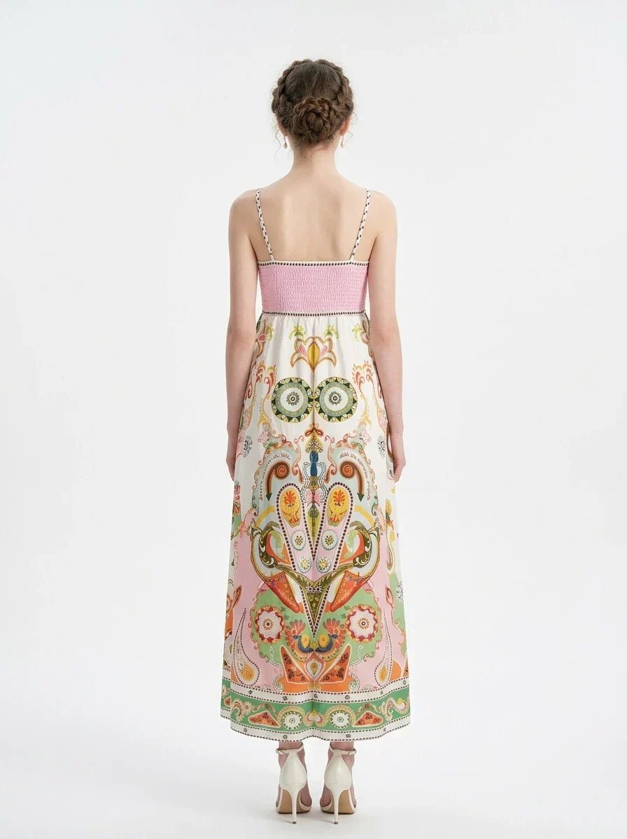 Rear view of a woman wearing a white maxi dress with a colorful paisley print and pink smocked bodice, standing against a white background.