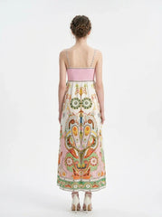 Rear view of a woman wearing a white maxi dress with a colorful paisley print and pink smocked bodice, standing against a white background.