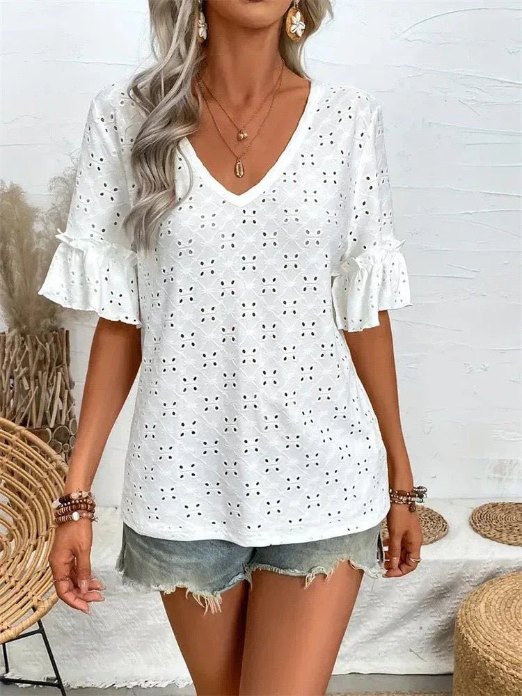A woman stands wearing a white eyelet top with ruffled short sleeves and denim shorts.