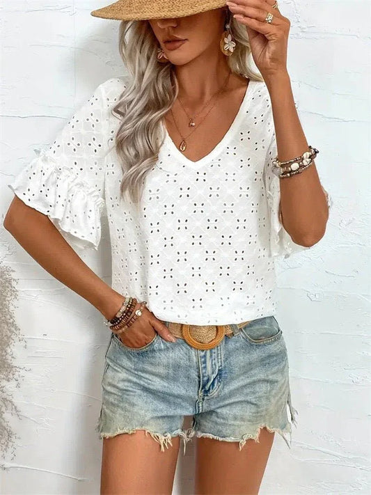 A woman wearing a white eyelet top with ruffled sleeves and denim shorts poses with a straw hat.