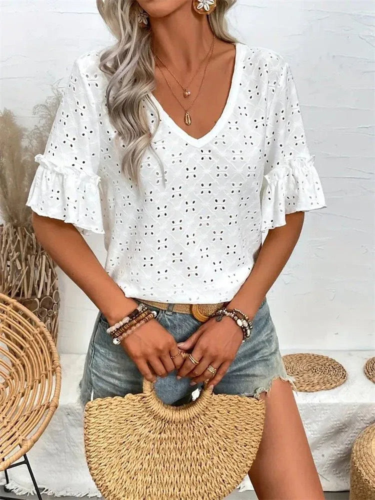 A woman holds a straw handbag while wearing a white eyelet top with ruffled sleeves and denim shorts.