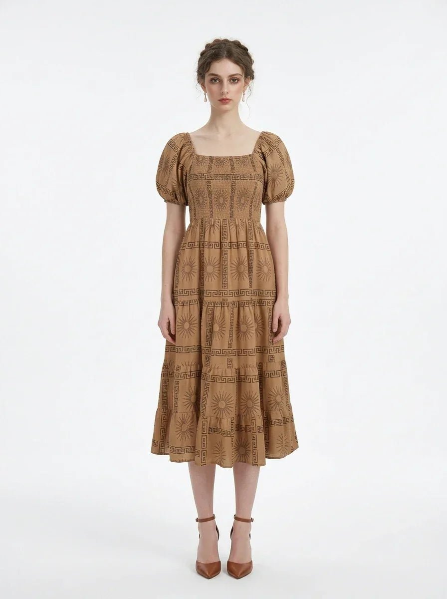 Woman wearing a brown puff-sleeve midi dress with a smocked bodice and tiered skirt featuring a sun and geometric print, standing against a white background.
