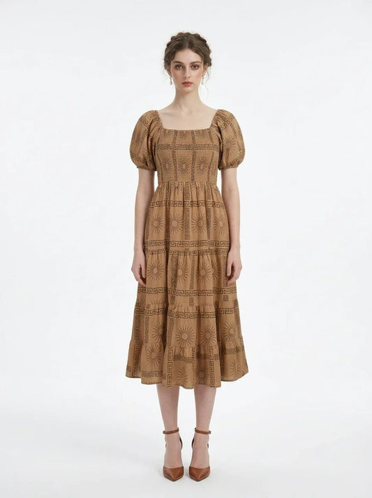 Woman wearing a brown puff-sleeve midi dress with a smocked bodice and tiered skirt featuring a sun and geometric print, standing against a white background.
